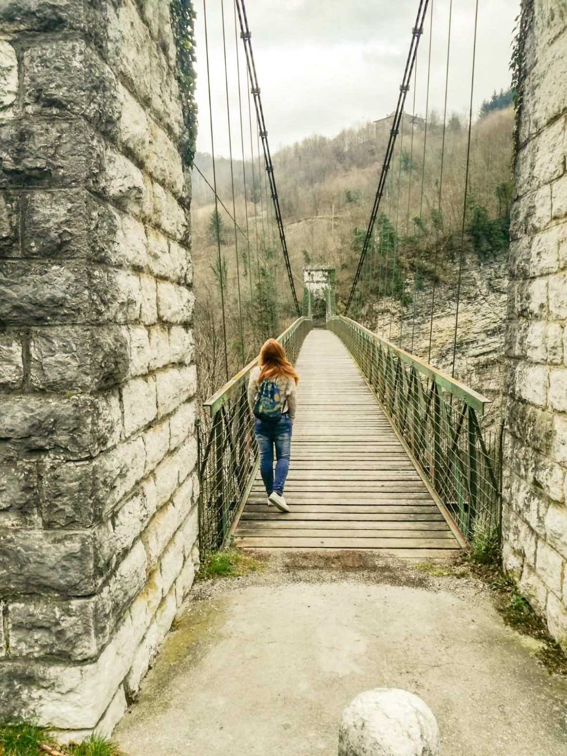 una ragazza bionda, con dei jeans e uno zainetto lungo il ponte di Arsiè