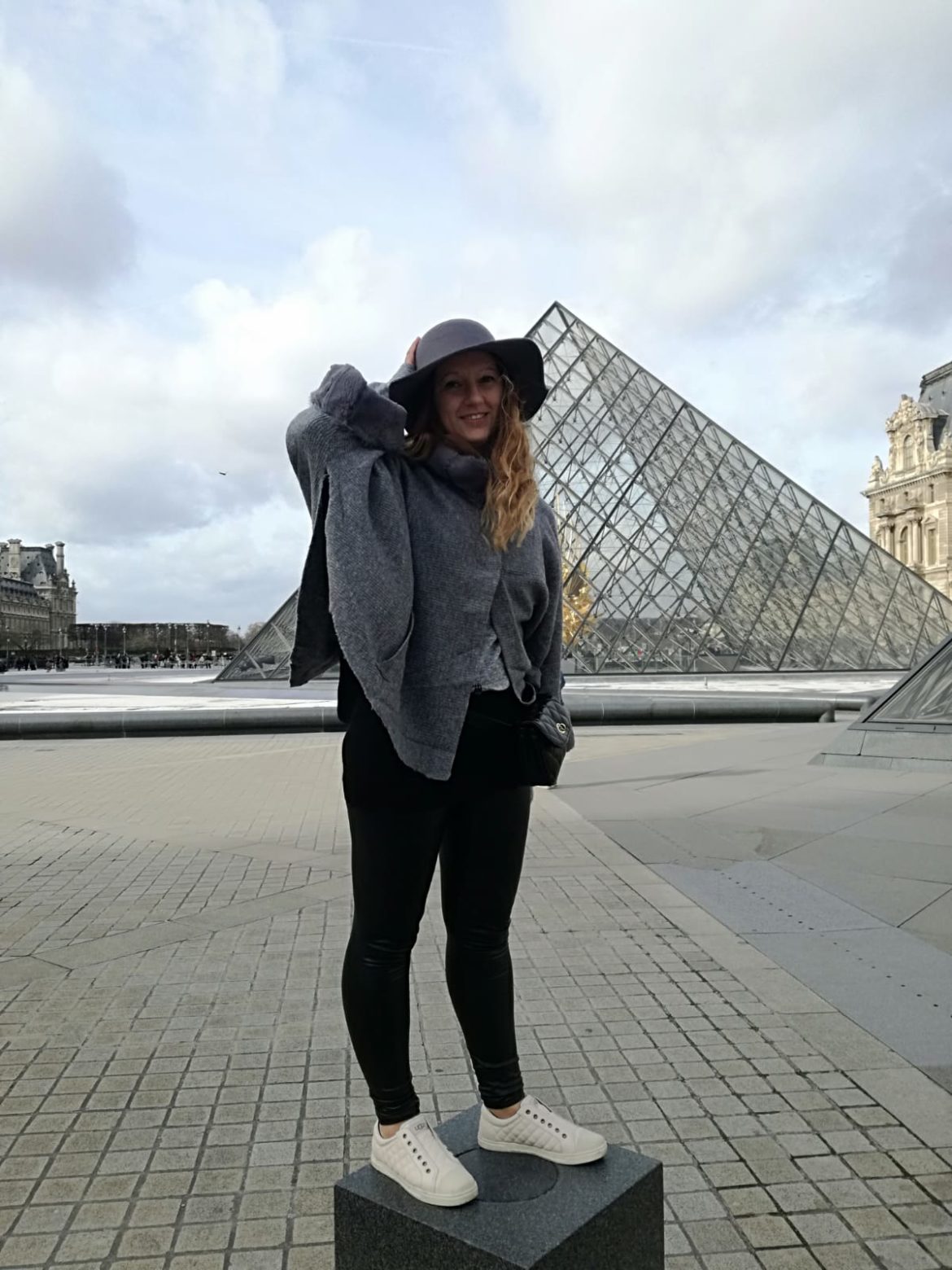 Una ragazza con il cappello e sullo sfondo una delle piramidi di vetro del Louvre